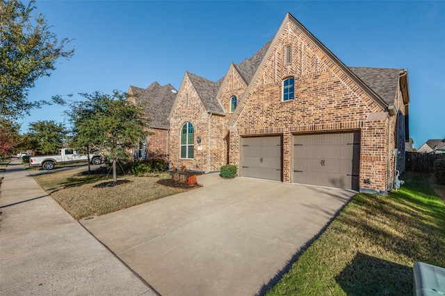 tudor house with a garage, brick siding, concrete driveway, and a front lawn