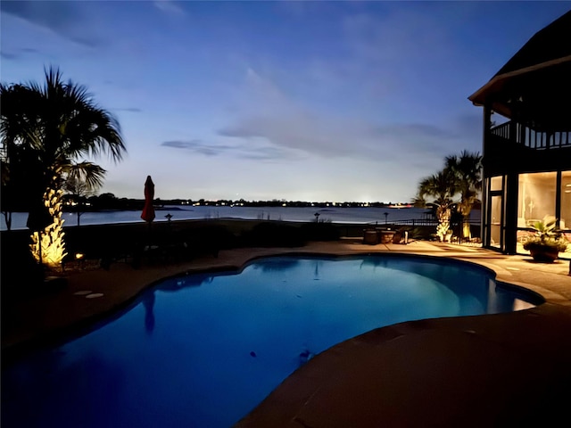 pool at dusk with a patio area and a water view