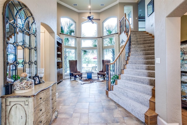 entryway with ceiling fan, ornamental molding, a high ceiling, and a wealth of natural light