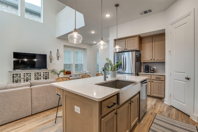 kitchen with stainless steel appliances, sink, light hardwood / wood-style flooring, hanging light fixtures, and an island with sink