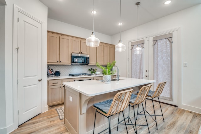 kitchen featuring appliances with stainless steel finishes, light brown cabinetry, sink, light hardwood / wood-style flooring, and an island with sink