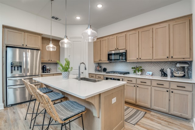 kitchen with appliances with stainless steel finishes, backsplash, sink, light hardwood / wood-style floors, and hanging light fixtures