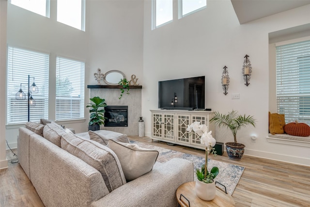 living room featuring a high ceiling, a tile fireplace, and light hardwood / wood-style flooring