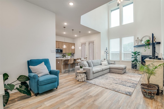 living room with ceiling fan, a towering ceiling, a wealth of natural light, and light hardwood / wood-style flooring