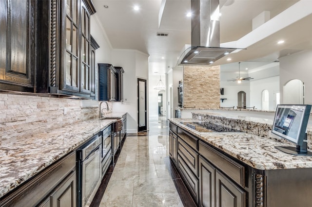 kitchen with ceiling fan, light stone countertops, ornamental molding, dark brown cabinets, and island exhaust hood