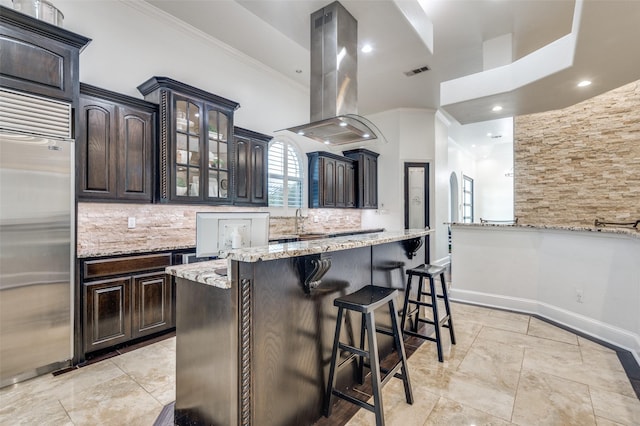 kitchen featuring light stone counters, high quality fridge, island range hood, a breakfast bar, and ornamental molding