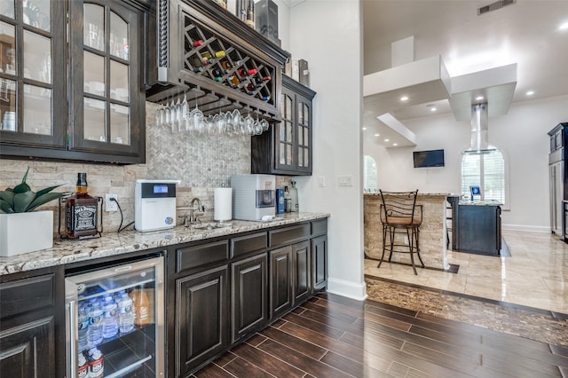 bar with decorative backsplash, light stone counters, dark wood-type flooring, and beverage cooler