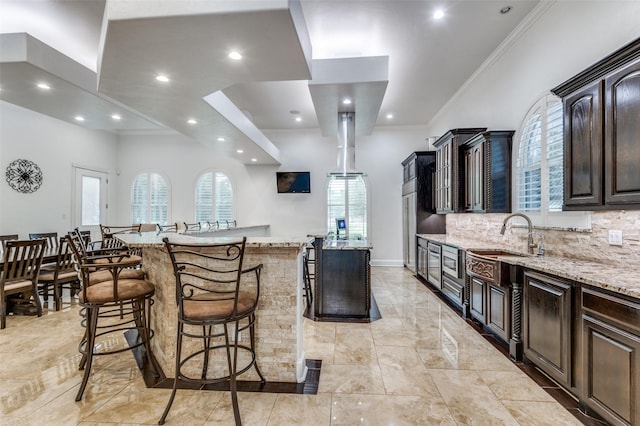 kitchen with backsplash, dark brown cabinetry, light stone countertops, and a kitchen island