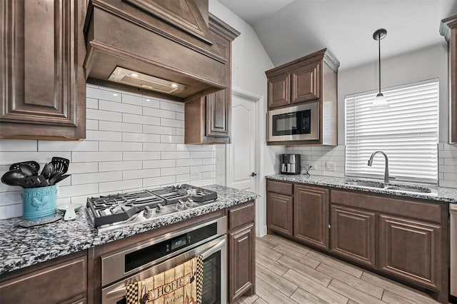 kitchen with sink, dark stone countertops, dark brown cabinetry, black appliances, and custom range hood