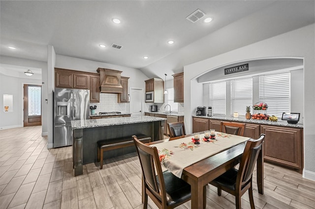 kitchen featuring appliances with stainless steel finishes, backsplash, custom exhaust hood, a center island, and light stone countertops