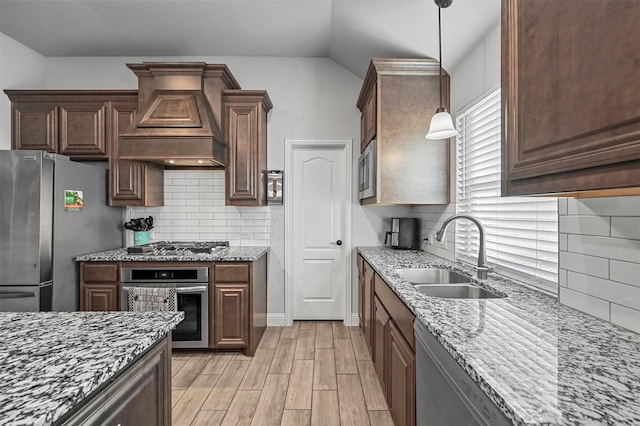 kitchen featuring sink, appliances with stainless steel finishes, light stone counters, custom range hood, and decorative light fixtures