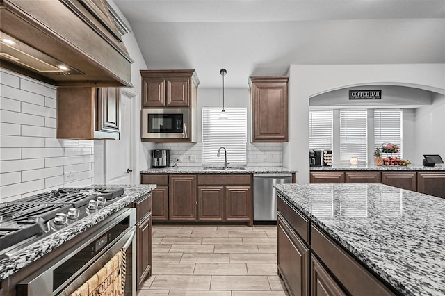 kitchen featuring built in microwave, sink, stainless steel dishwasher, light stone counters, and custom range hood