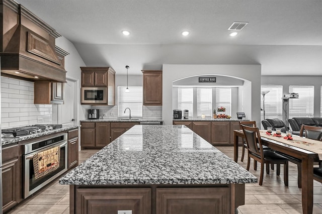 kitchen featuring hanging light fixtures, stainless steel appliances, a center island, and premium range hood