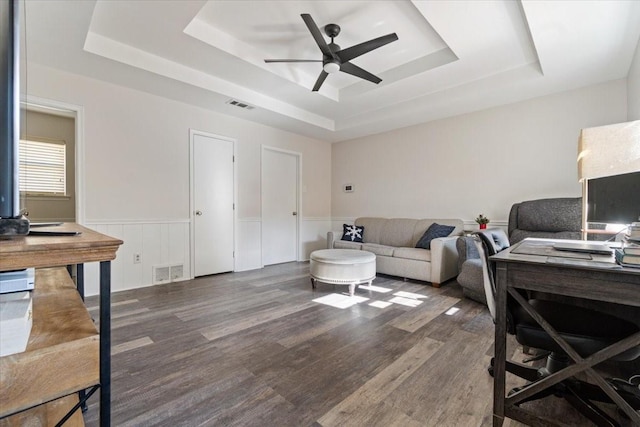 living room featuring ceiling fan, dark hardwood / wood-style flooring, and a tray ceiling