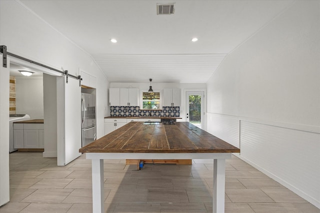 unfurnished dining area featuring a barn door, washer / clothes dryer, and vaulted ceiling