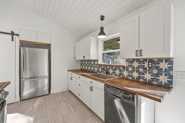 kitchen featuring lofted ceiling, sink, a barn door, appliances with stainless steel finishes, and butcher block counters