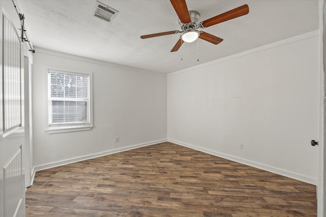 unfurnished room featuring a textured ceiling, a barn door, ceiling fan, and dark wood-type flooring