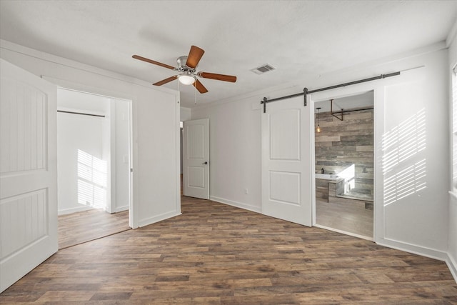 unfurnished bedroom featuring ceiling fan, ornamental molding, a barn door, and dark hardwood / wood-style flooring