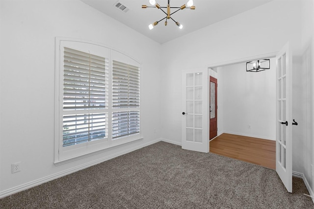 carpeted spare room featuring a chandelier and french doors