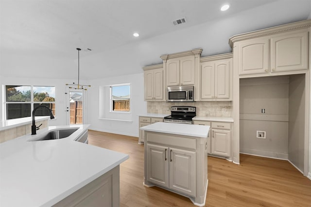 kitchen featuring appliances with stainless steel finishes, sink, decorative light fixtures, cream cabinetry, and a kitchen island