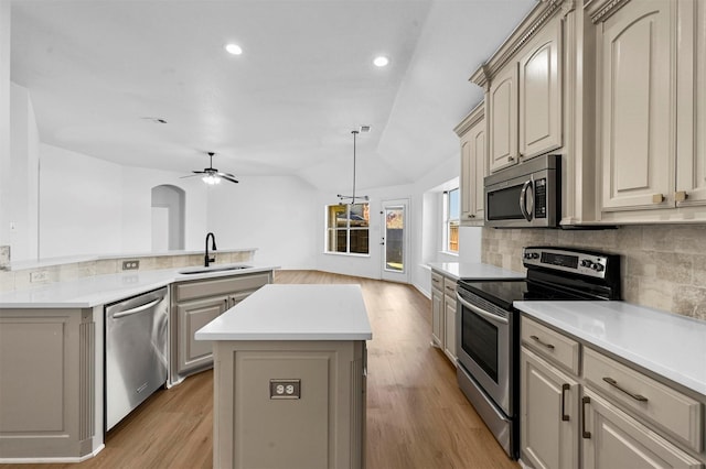 kitchen featuring appliances with stainless steel finishes, a center island, lofted ceiling, sink, and backsplash