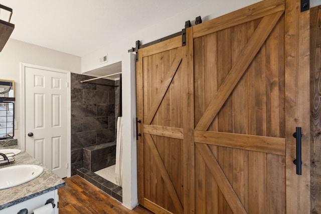 bathroom featuring a tile shower, vanity, and wood-type flooring