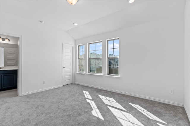 unfurnished bedroom featuring light carpet, ensuite bath, and lofted ceiling