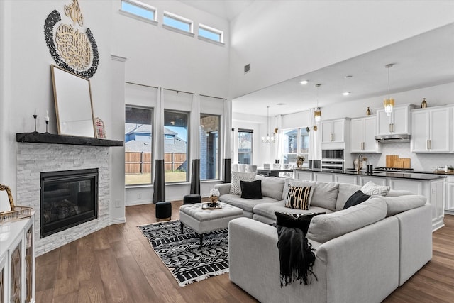 living room featuring a fireplace, a towering ceiling, dark wood-type flooring, and sink