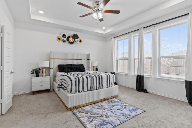 carpeted bedroom with ceiling fan, a tray ceiling, and multiple windows