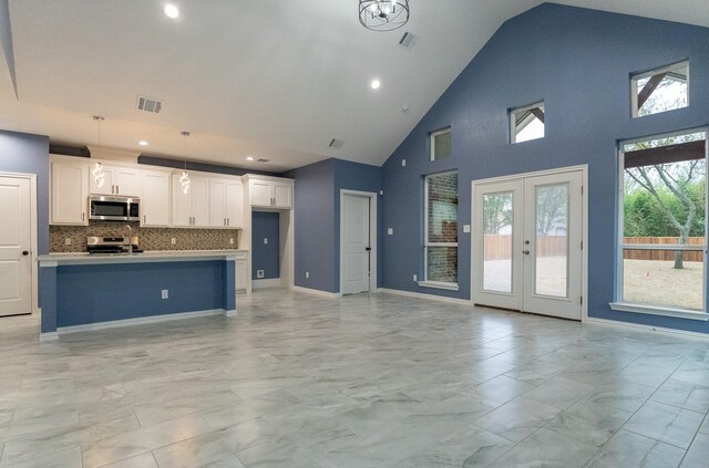 kitchen with decorative light fixtures, white cabinetry, stainless steel appliances, a kitchen island with sink, and high vaulted ceiling