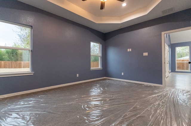 unfurnished room featuring ceiling fan, a wealth of natural light, and a tray ceiling