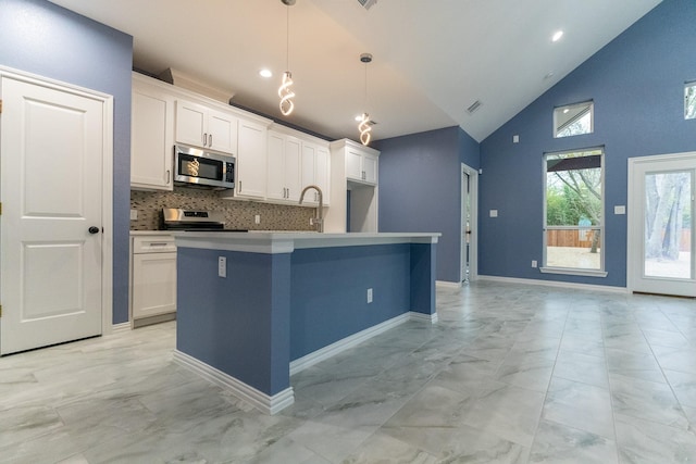 kitchen featuring hanging light fixtures, white cabinets, a kitchen island with sink, and appliances with stainless steel finishes