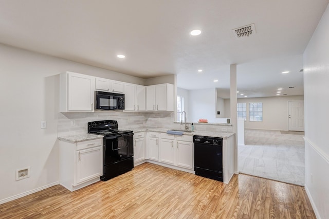 kitchen with sink, tasteful backsplash, white cabinets, black appliances, and light wood-type flooring