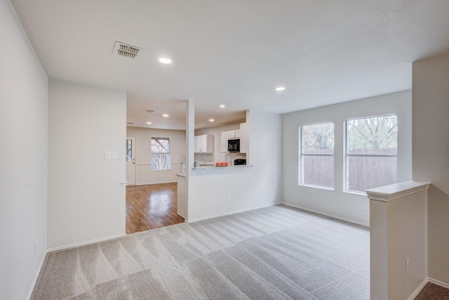 unfurnished living room with light colored carpet and a wealth of natural light