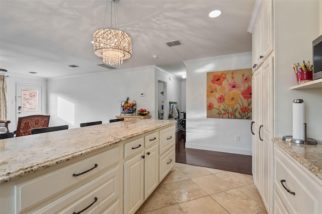 kitchen with light tile patterned floors, crown molding, hanging light fixtures, light stone counters, and cream cabinets