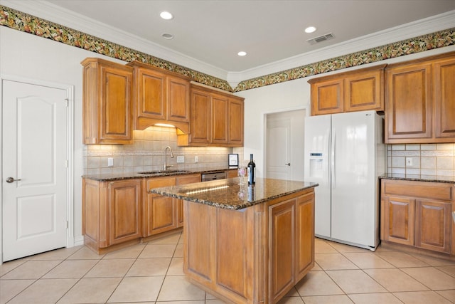 kitchen featuring dark stone counters, crown molding, sink, white refrigerator with ice dispenser, and a kitchen island