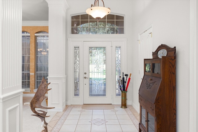 entrance foyer featuring light tile patterned floors, a towering ceiling, ornate columns, and crown molding