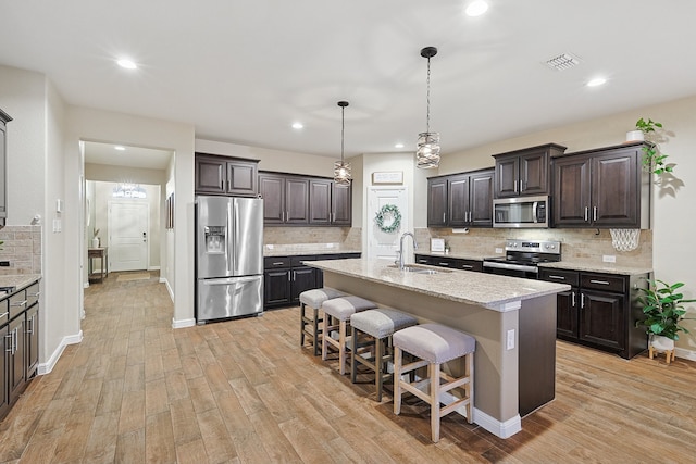 kitchen featuring sink, an island with sink, light hardwood / wood-style floors, and appliances with stainless steel finishes