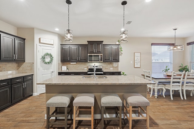 kitchen with appliances with stainless steel finishes, light hardwood / wood-style floors, a kitchen island with sink, and sink