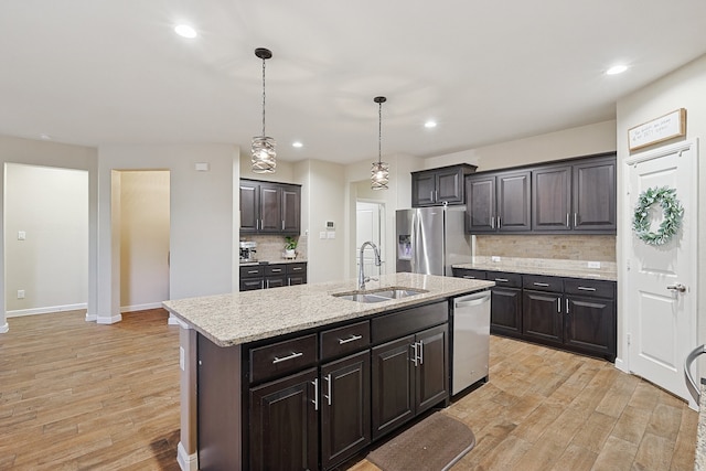 kitchen featuring sink, an island with sink, appliances with stainless steel finishes, tasteful backsplash, and decorative light fixtures