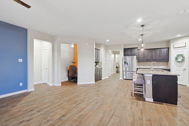 kitchen with stainless steel fridge, tasteful backsplash, sink, light hardwood / wood-style flooring, and an island with sink