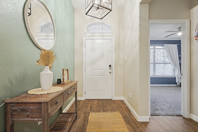 entryway with ceiling fan with notable chandelier, crown molding, and dark wood-type flooring