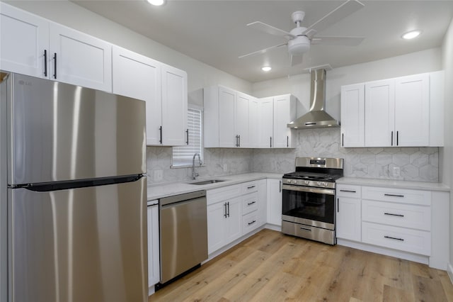 kitchen featuring white cabinets, wall chimney range hood, sink, light hardwood / wood-style flooring, and appliances with stainless steel finishes