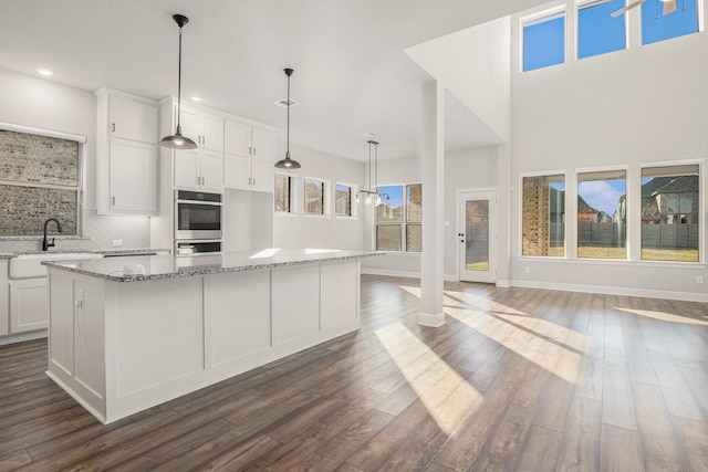 kitchen with sink, a kitchen island, pendant lighting, light stone countertops, and white cabinets