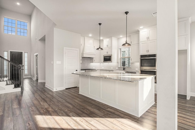 kitchen with a center island, white cabinets, light stone counters, and custom range hood