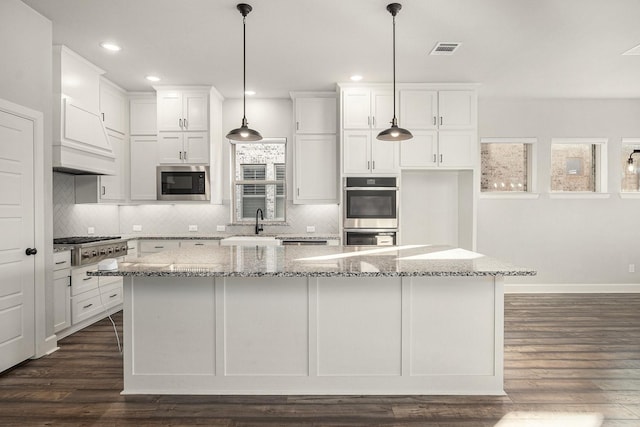 kitchen featuring a large island, appliances with stainless steel finishes, hanging light fixtures, dark hardwood / wood-style floors, and light stone counters