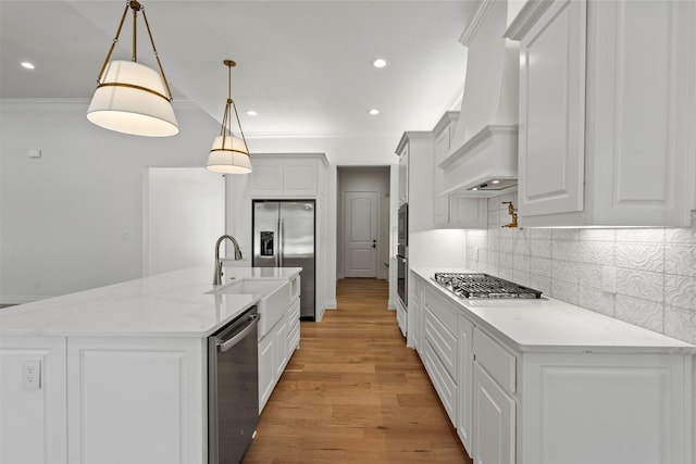 kitchen featuring a kitchen island with sink, premium range hood, appliances with stainless steel finishes, decorative light fixtures, and light stone counters