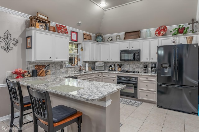 kitchen featuring kitchen peninsula, a kitchen bar, white cabinets, and black appliances