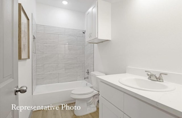 full bathroom with hardwood / wood-style flooring, tiled shower / bath, vanity, and toilet