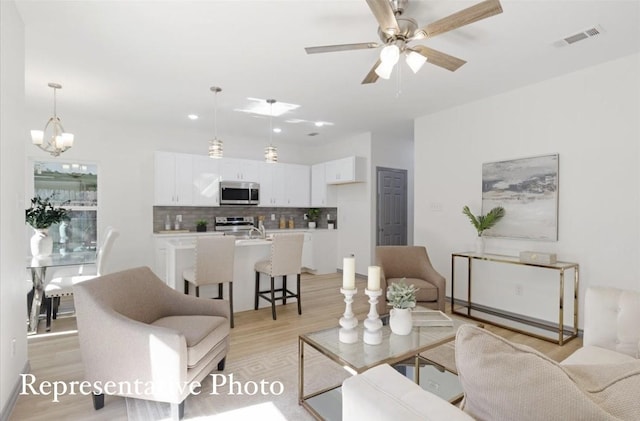 living room featuring ceiling fan with notable chandelier and light hardwood / wood-style floors